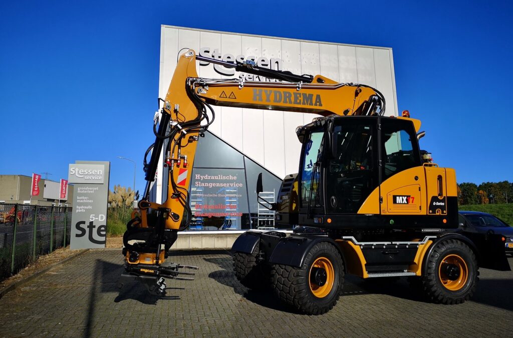 Gele Hydrema graafmachine die voor het gebouw staat van E&R Stessen.